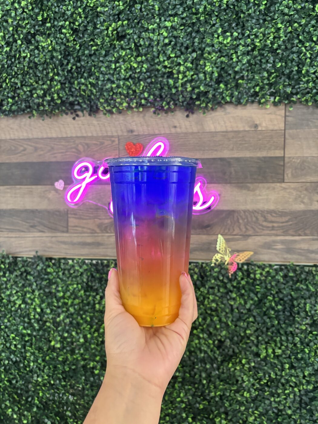 Layered rainbow energy tea in front of the green hedge wall and pink Good Vibes neon at Casa Grande Nutrition